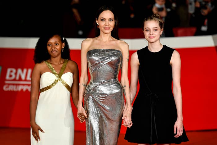 Two people in elegant red carpet gowns and another in a black dress, all posing together