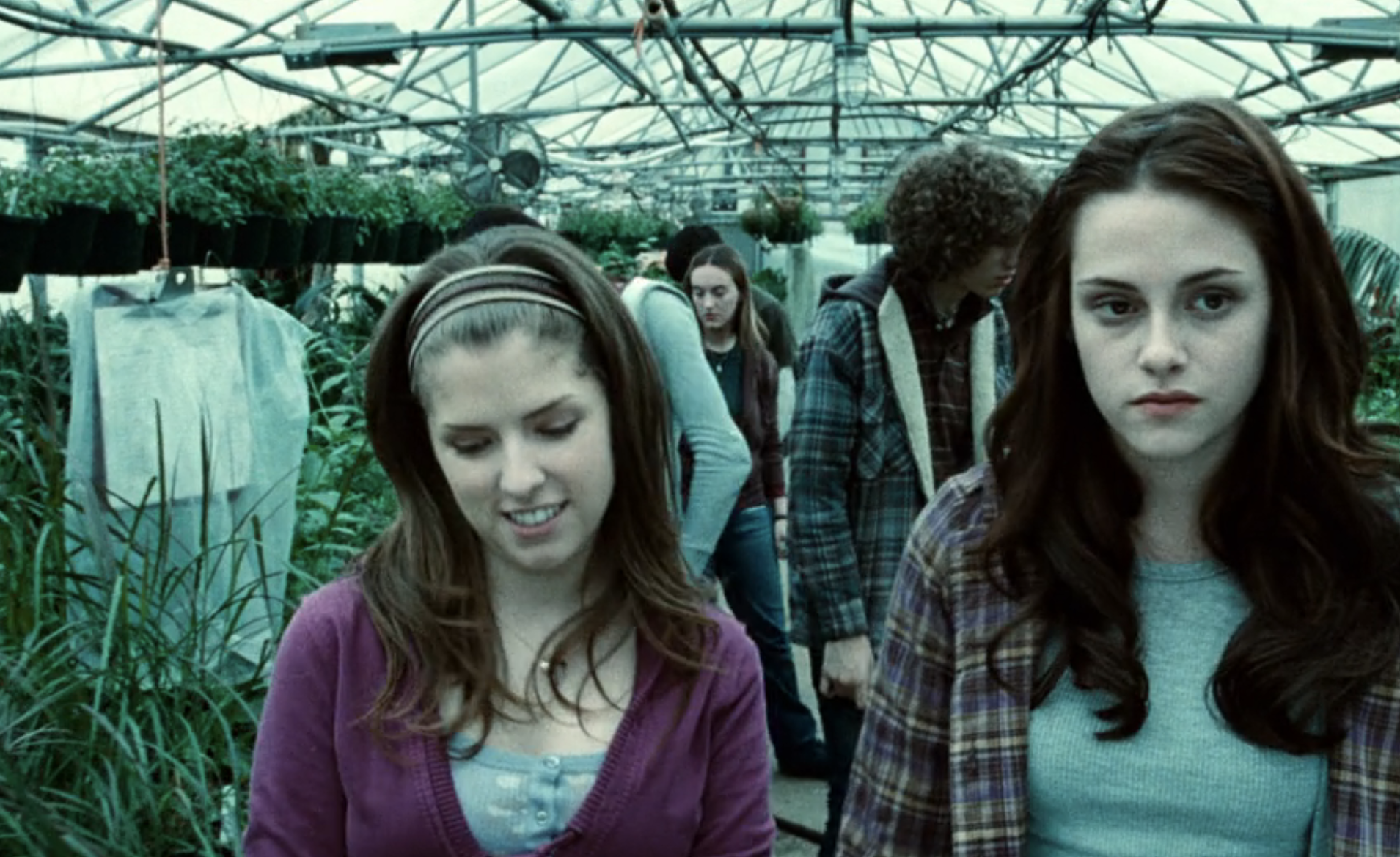 Anna Kendrick and Kristen Stewart walking in a greenhouse surrounded by plants in a scene from a movie