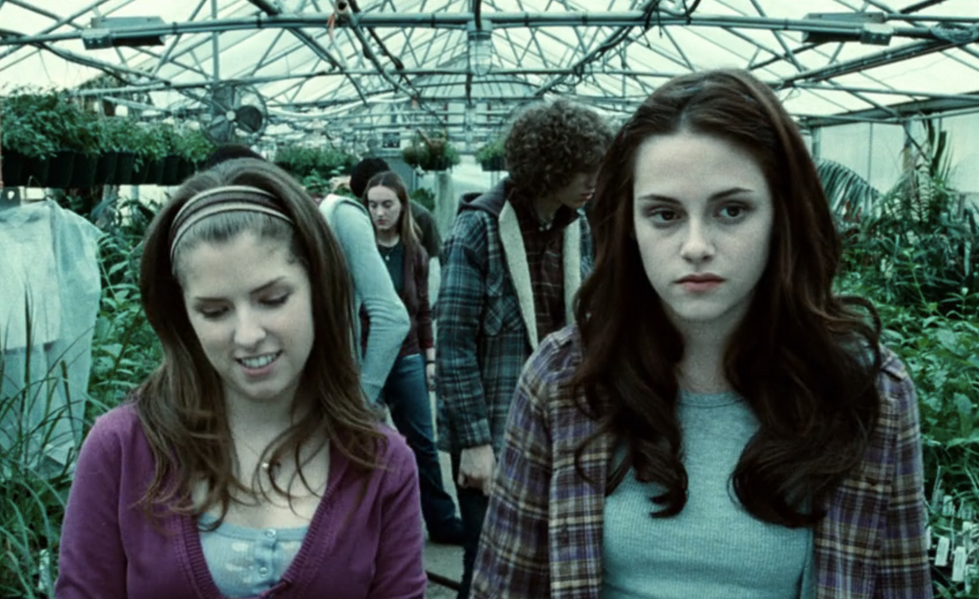 Anna Kendrick and Kristen Stewart walking in a greenhouse surrounded by plants in a scene from a movie