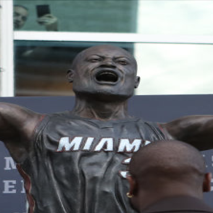 Statue of a basketball player in a triumphant pose outside a building, with onlookers in the background