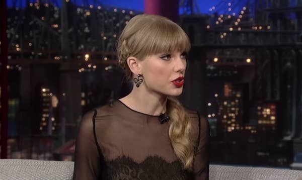 A woman with a braided hairstyle in a sheer lace dress sits on a talk show set, engaging in conversation