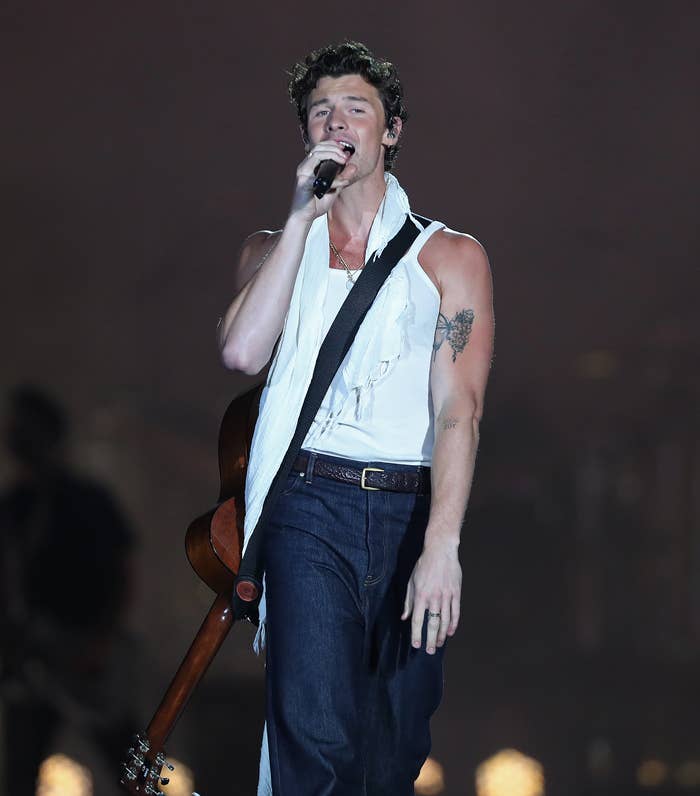 Shawn Mendes singing onstage with a guitar slung across his back