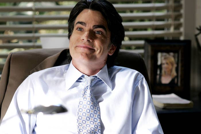 Sandy Cohen in an office smiling, wearing a suit and patterned tie; photo in background on desk