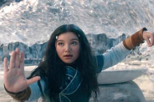 A girl dressed in fantasy warrior attire stands looking intense, with one hand raised in a gesture, in a dramatic icy landscape