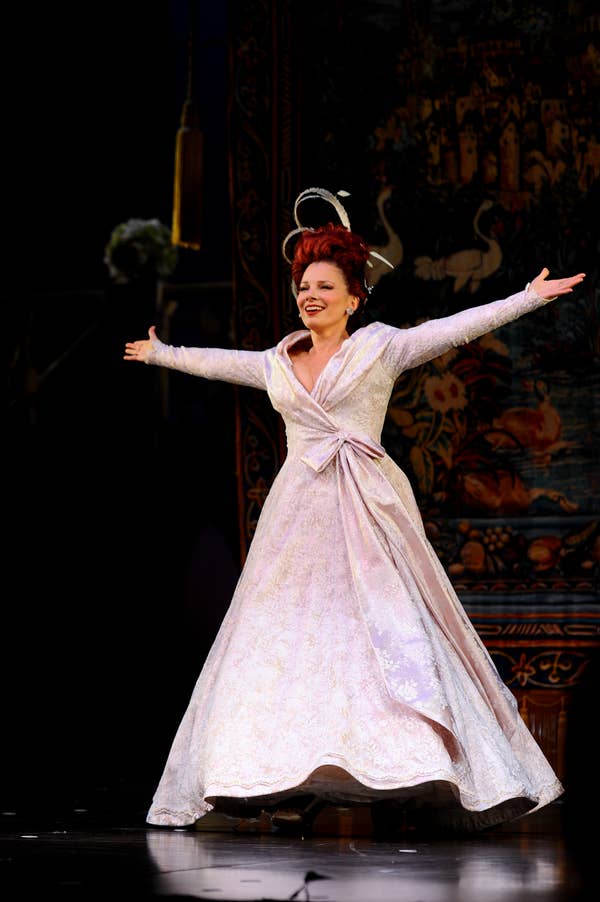 Fran on stage wears an elaborate gown with wide sleeves and a headpiece, arms outstretched