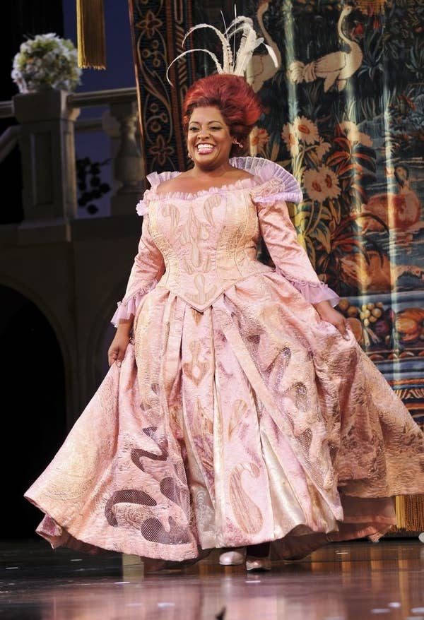 Sherri in an elaborate stage costume with ornate patterns, resembling a fairytale character, stands on a theatrical set