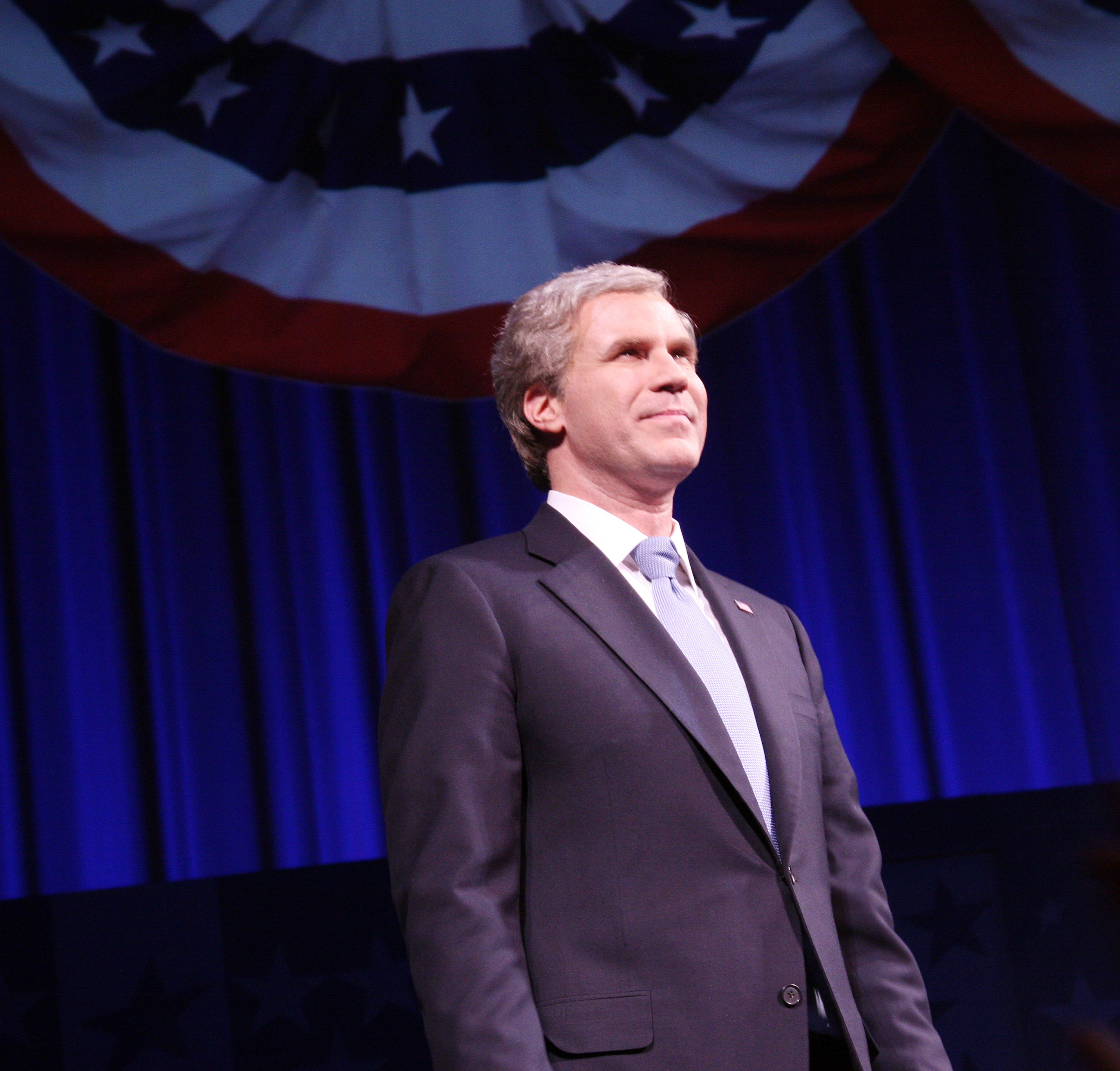 Will in a suit and wig stands on stage with star-patterned banners above