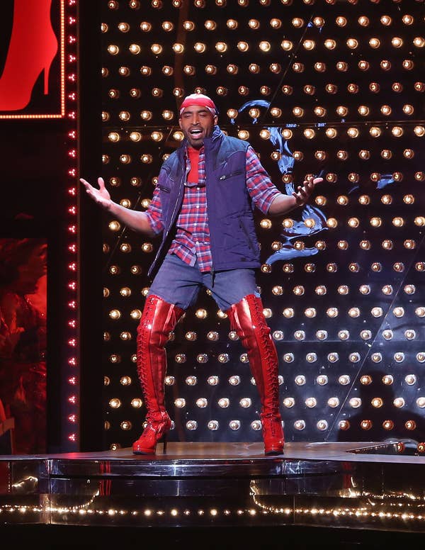 Tiki performing on stage in a plaid shirt, vest, and laced up thigh high boots