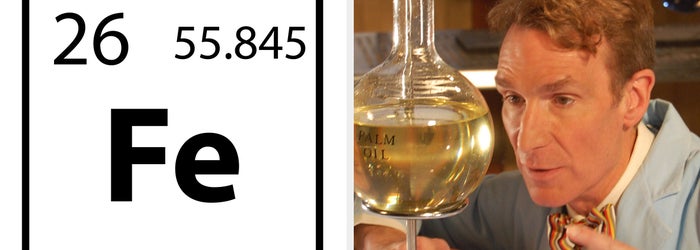 A scientist wearing a lab coat, gloves, and safety goggles carefully transfers liquid using a pipette into a test tube in a laboratory setting