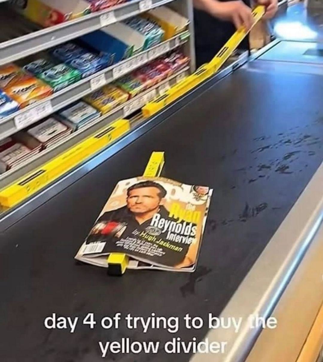 Checkout conveyor with magazine featuring Hugh Jackman. Caption: &quot;day 4 of trying to buy the yellow divider.&quot;