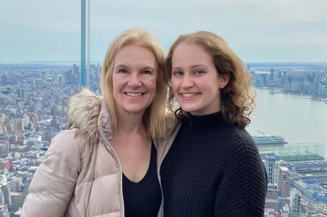 Two women smiling while standing together with a cityscape and river in the background