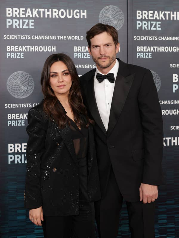 A woman in a black sequined suit and a man in a tuxedo pose together at a red carpet event with a &quot;Breakthrough Prize&quot; backdrop