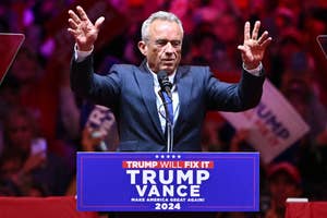 RFK Jr. speaks at a podium with "Trump Vance 2024" signage, surrounded by a crowd holding signs