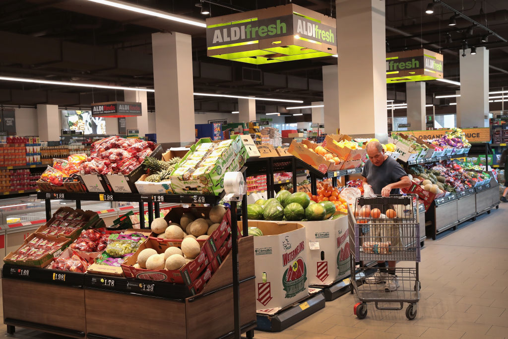 A person shops in a produce section at Aldi, selecting fruits and vegetables