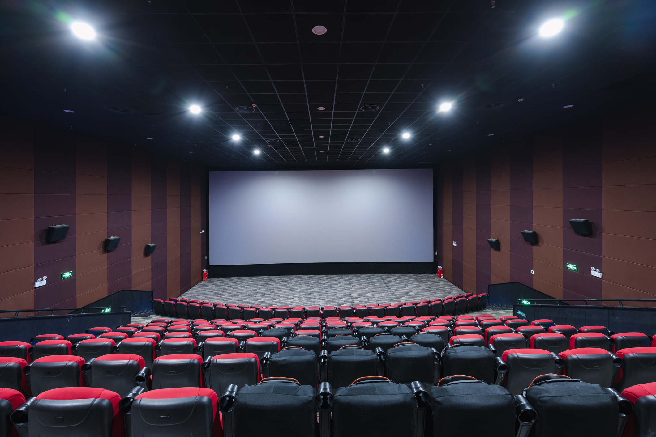 Empty movie theater with rows of red and black seats facing a large screen, surrounded by sound speakers on the walls