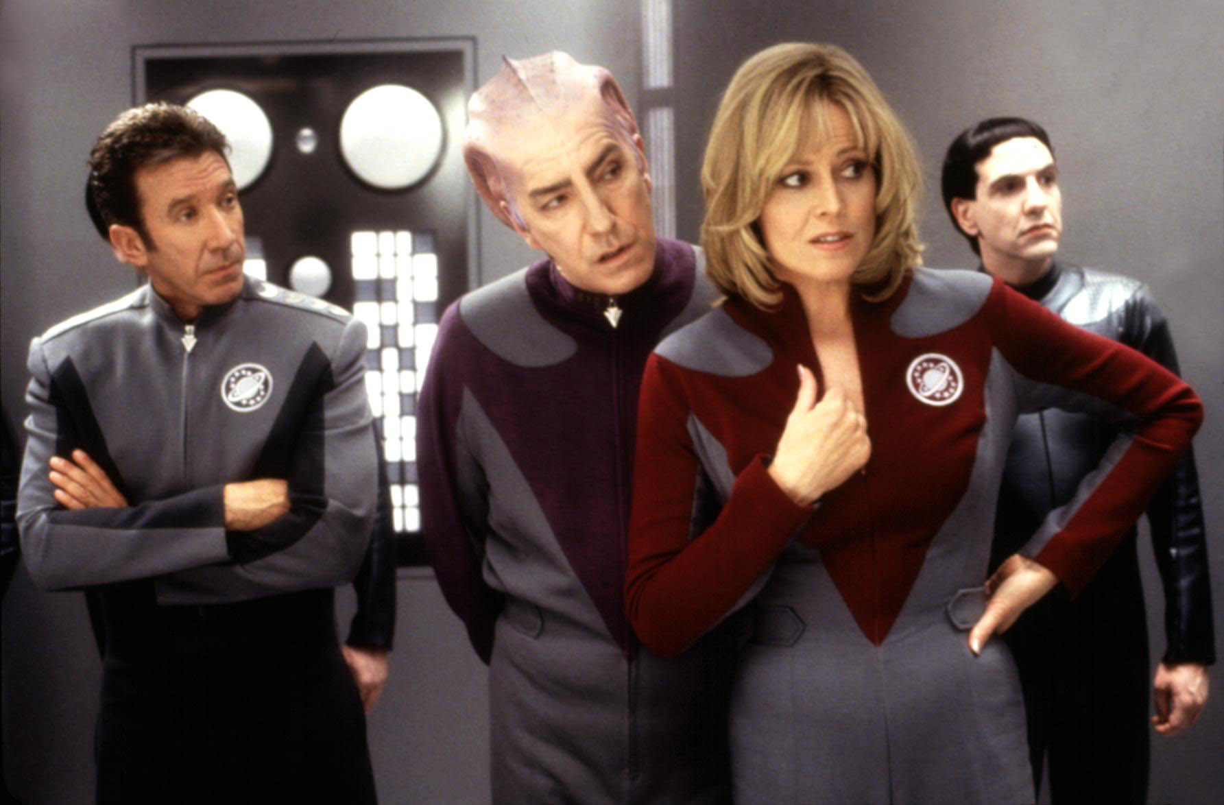 Four actors in sci-fi uniforms stand in a spaceship set, looking confused and focused