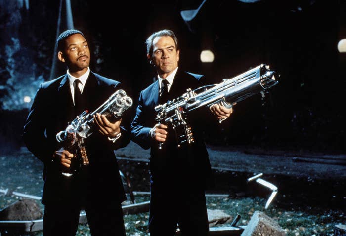 Two men in suits holding futuristic weapons in a night scene