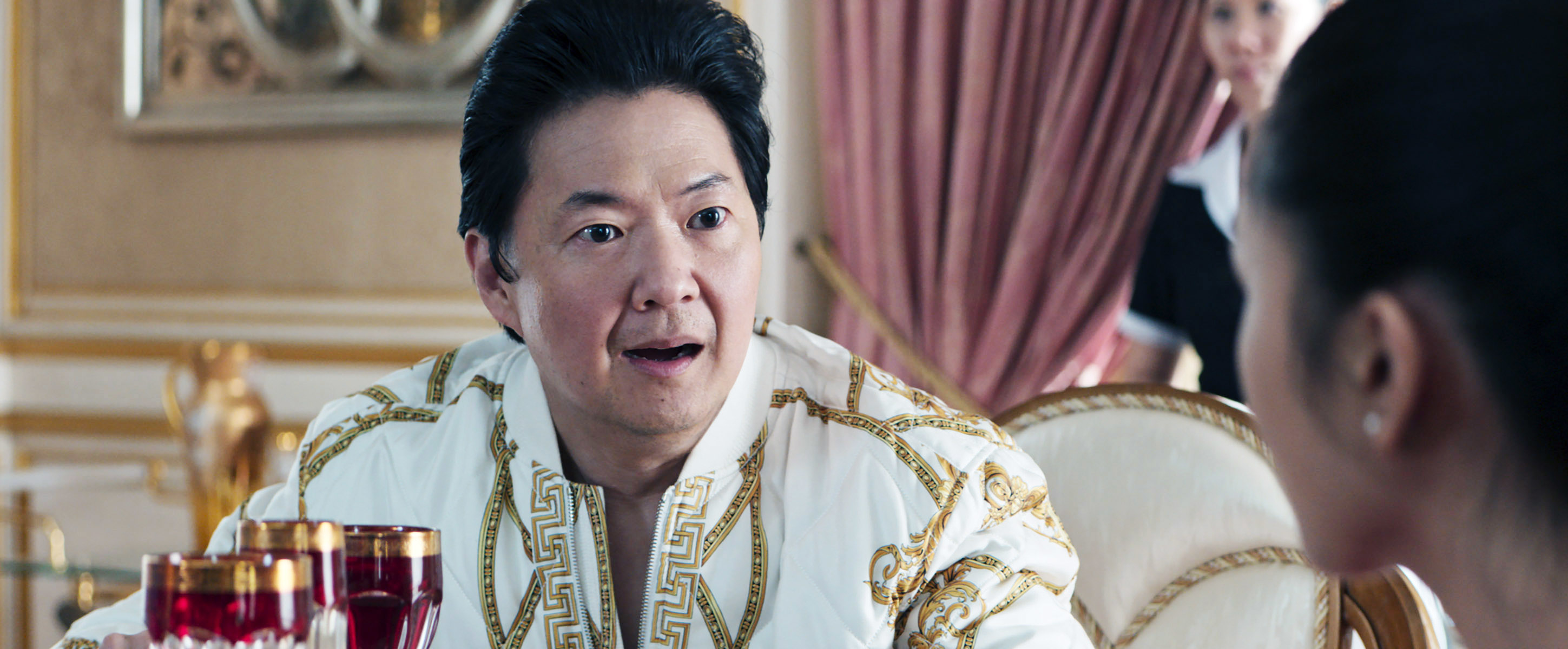 Ken in ornate, embroidered clothing reacts with surprise across a lavish table setting