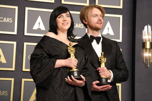 Two people holding awards on a stage, dressed in elegant formalwear