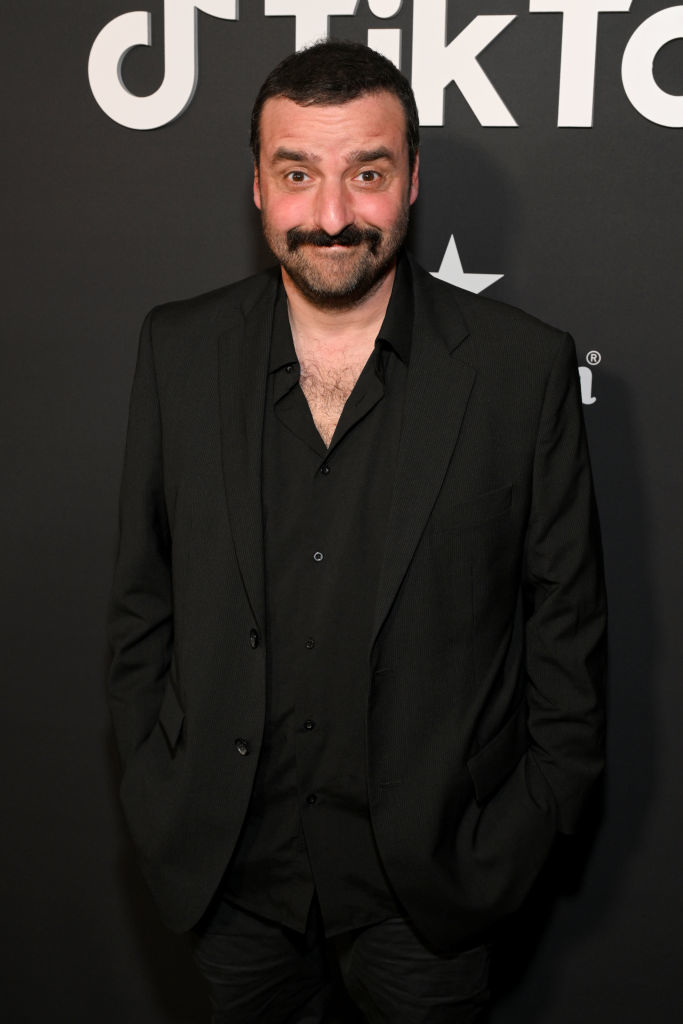 David posing on a red carpet, wearing a suit with an open-collared shirt