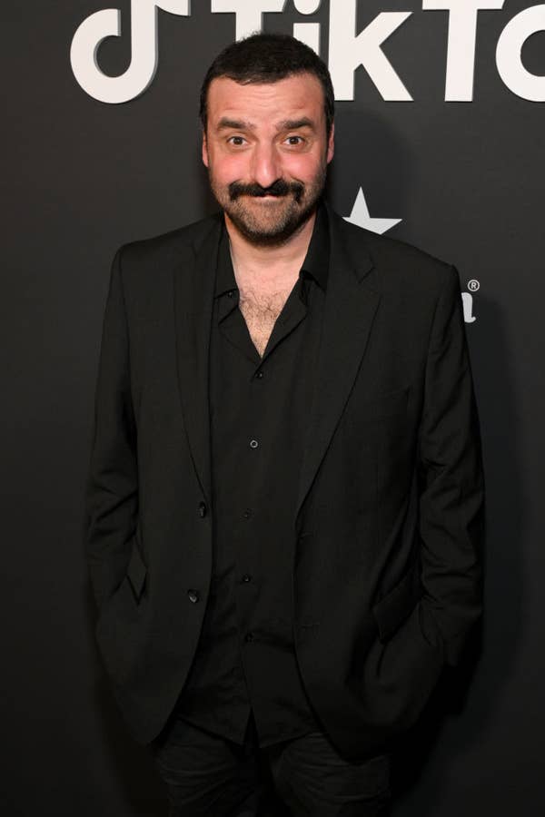 David posing on a red carpet, wearing a suit with an open-collared shirt