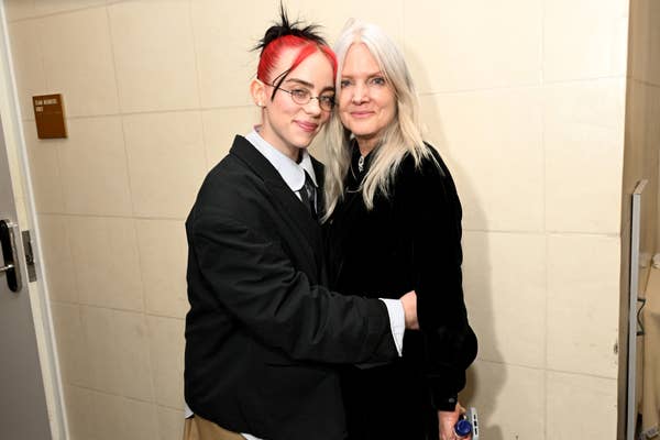 Two people hugging; one wears a suit jacket and glasses, the other a long black coat. Both appear happy. Names not provided