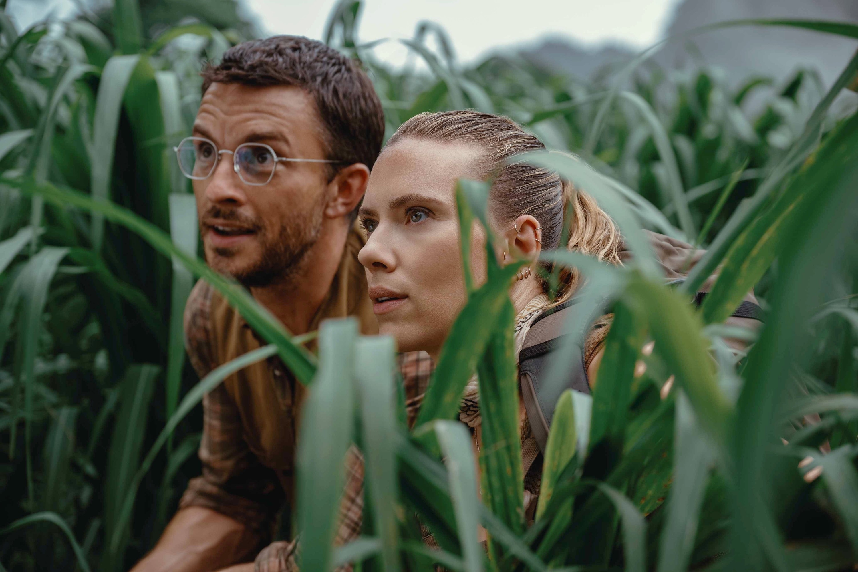 Jonathan Bailey and Scarlett Johansson crouching in tall grass, looking focused and adventurous