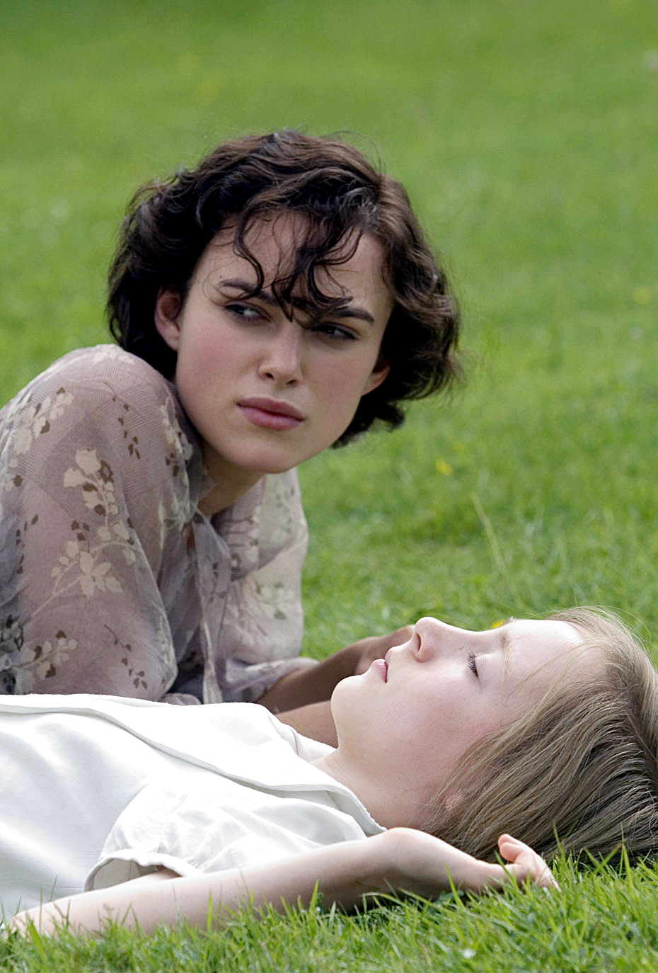 Keira and Saoirse are lying on the grass, one looking ahead and the other lying back with eyes closed