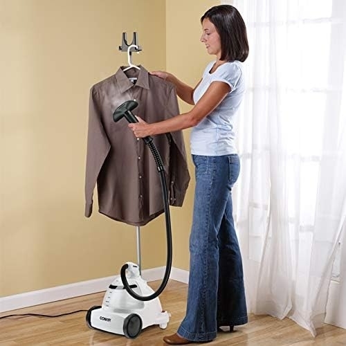 A person uses a clothing steamer to remove wrinkles from a shirt on a garment rack in a home setting