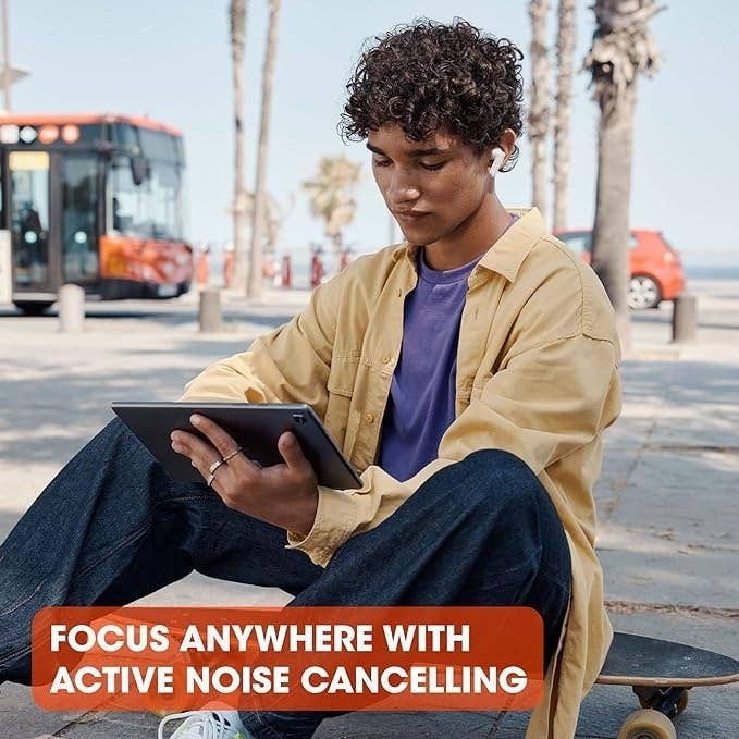 Person sitting on a skateboard, wearing headphones and reading a tablet. Background shows a bus and palm trees. Text: &quot;Focus anywhere with active noise cancelling.&quot;
