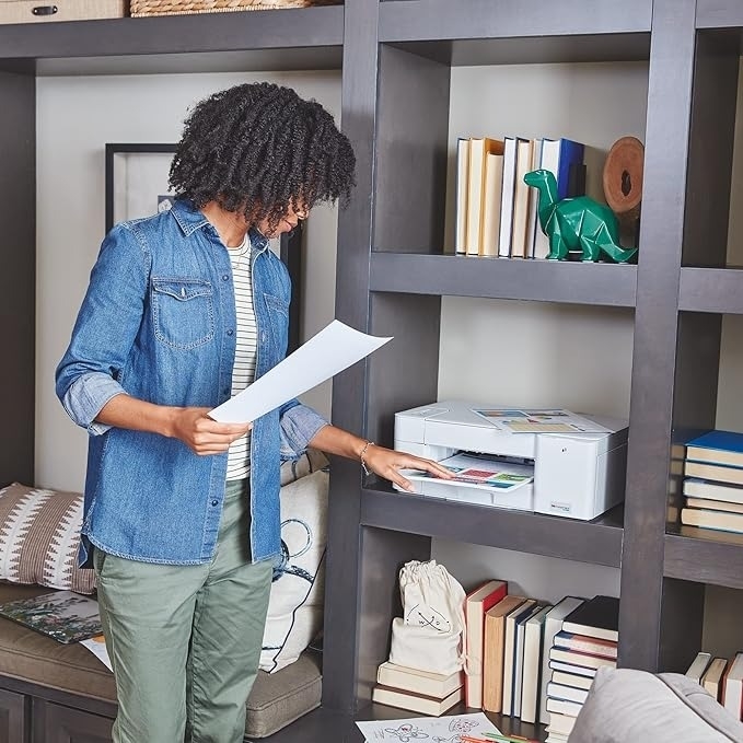 Person using a home printer to print color pages, with books and decor on shelves in the background