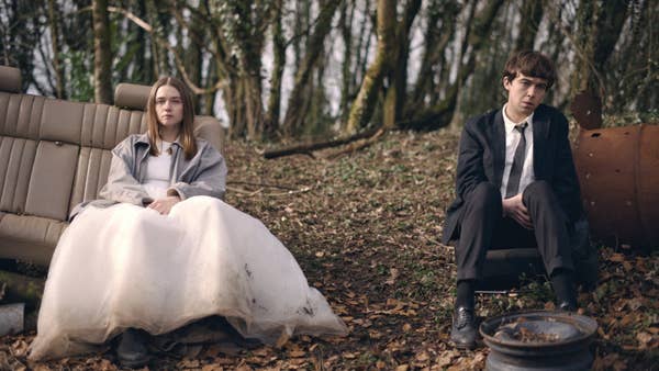 Two young adults sit in a wooded area on makeshift seats, wearing formal attire