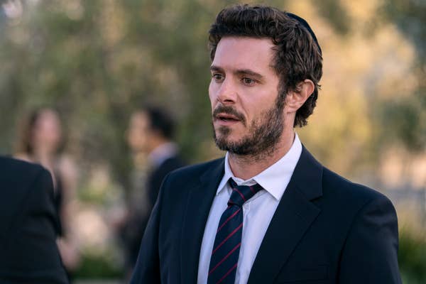 A man in a suit with a tie, outdoors, looking thoughtful