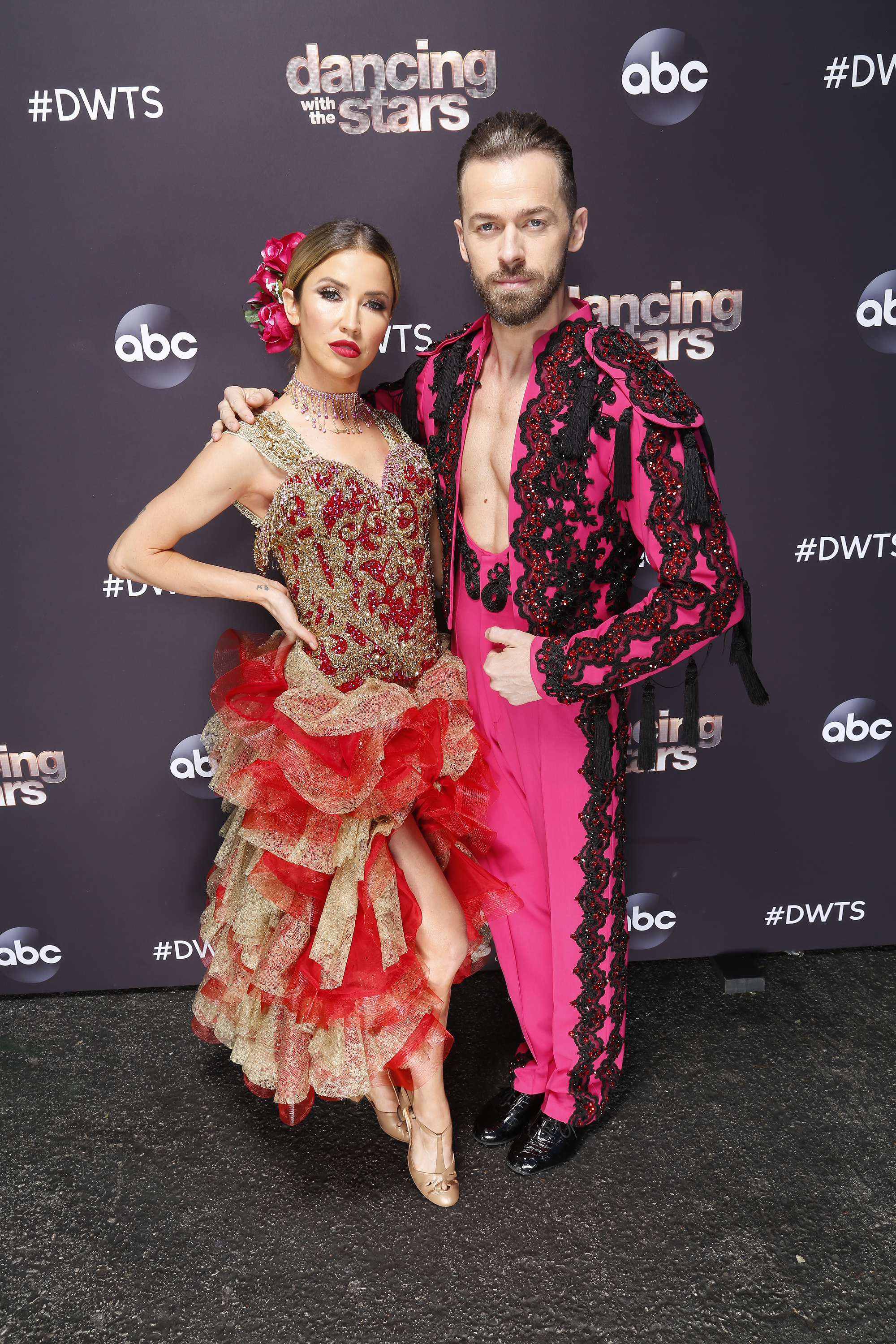 Kaitlyn Bristowe and Artem Chigvintsev in dance attire pose on the &quot;Dancing With the Stars&quot; red carpet. The woman wears a ruffled dress; the man sports an ornate jacket and pants