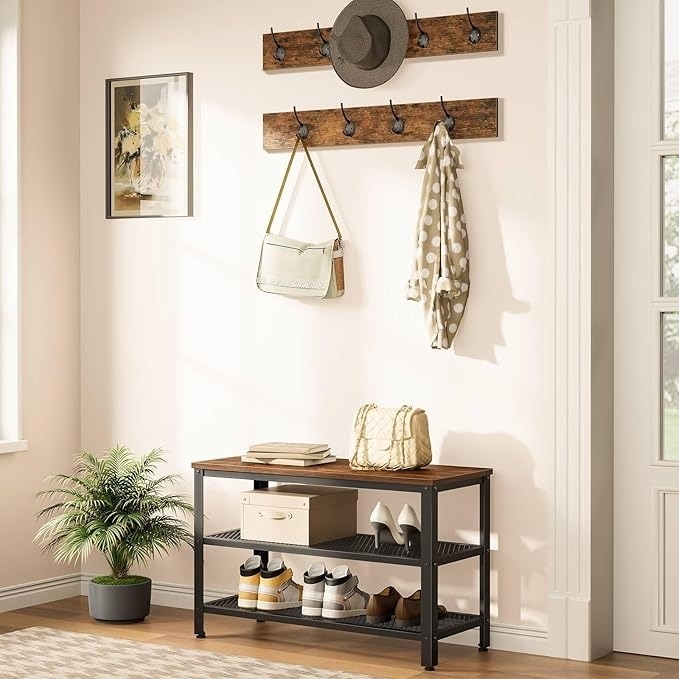 Entryway with wall hooks holding a hat, bag, and scarf; below is a bench with storage shelves featuring boxes and another bag