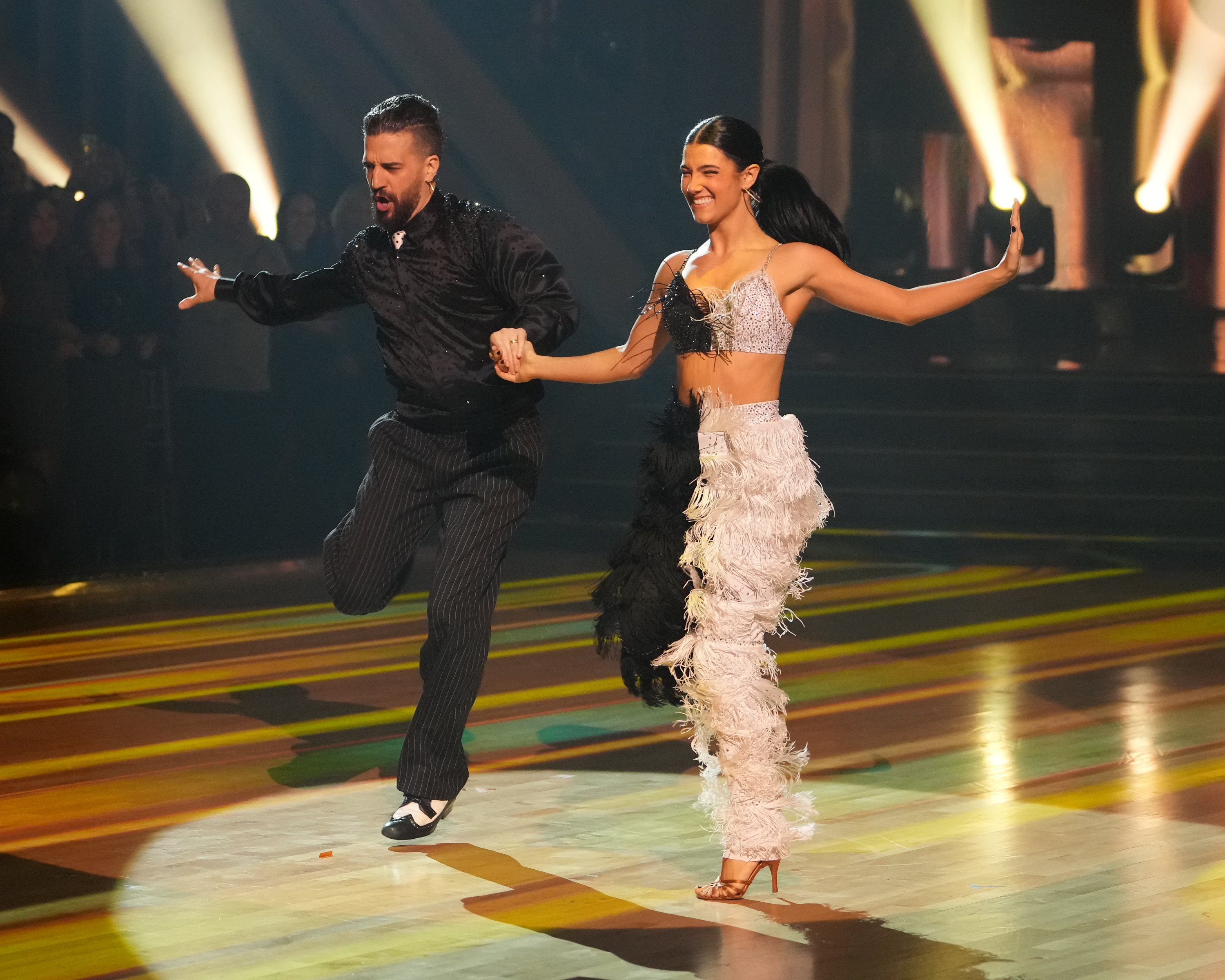 Charli D&#x27;Amelio and Mark Ballas perform energetically on a dance floor. The woman wears a glamorous feathery outfit.