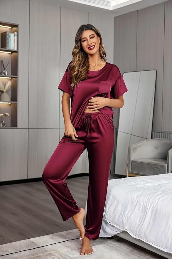 Person in satin pajamas stands in a bedroom, smiling. Fashionable loungewear showcased