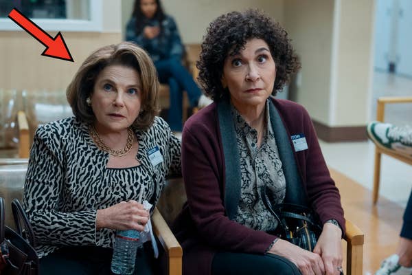 Two women sitting in a waiting room, one with a leopard-patterned blouse and the other in a maroon cardigan, looking attentive