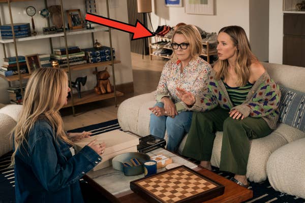 Two women on a couch, one wearing a floral shirt and glasses, the other in a striped top and cardigan, talk to a third woman across from them in a modern living room
