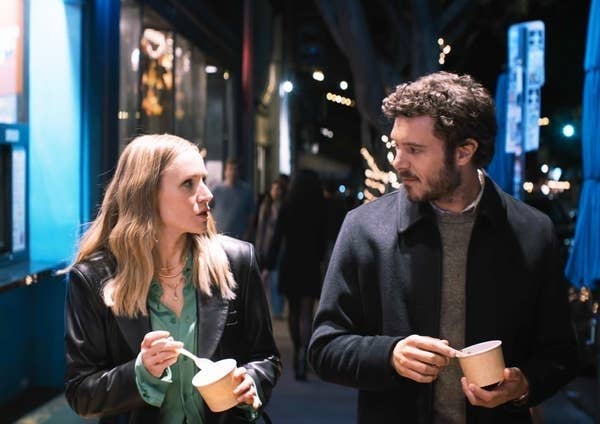 Two people enjoy ice cream on a city sidewalk at night, engaged in conversation