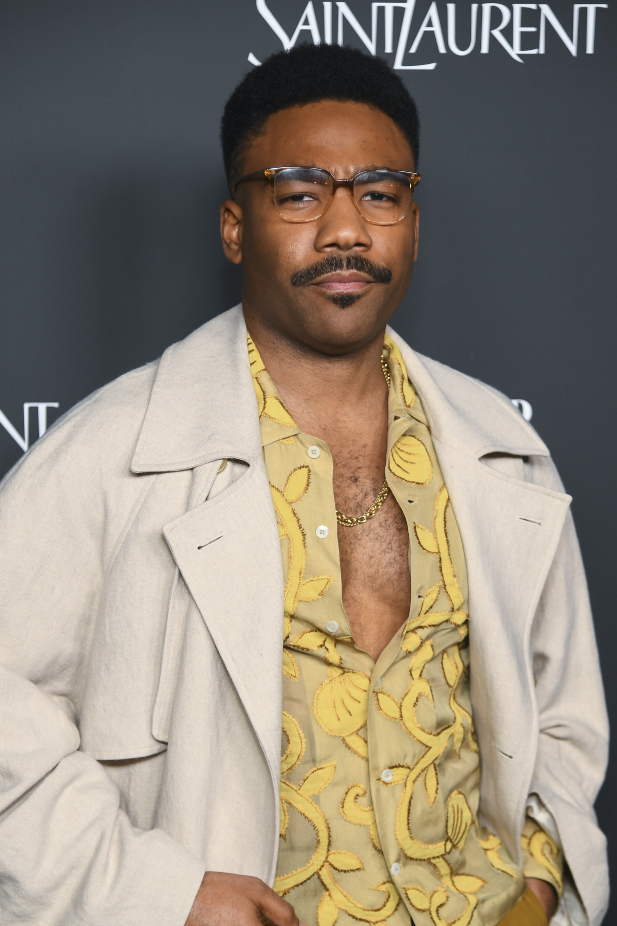 A person in a patterned shirt and light coat attends a Saint Laurent event