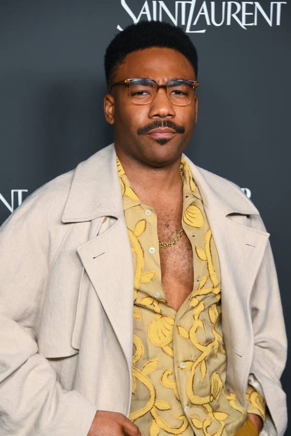 A person in a patterned shirt and light coat attends a Saint Laurent event