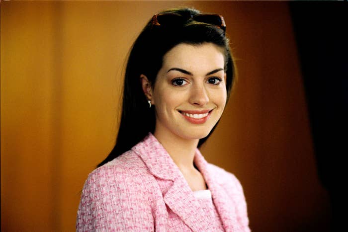 A woman with long dark hair smiles while wearing a textured pink jacket and sunglasses on her head