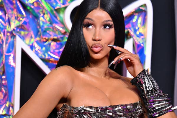 Cardi B touches her face while making a kissy face in a metallic dress on the red carpet