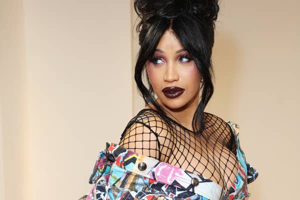 Cardi B in a graffiti inspired dress with fishnets and fishnet stockings with her hair in a tall updo