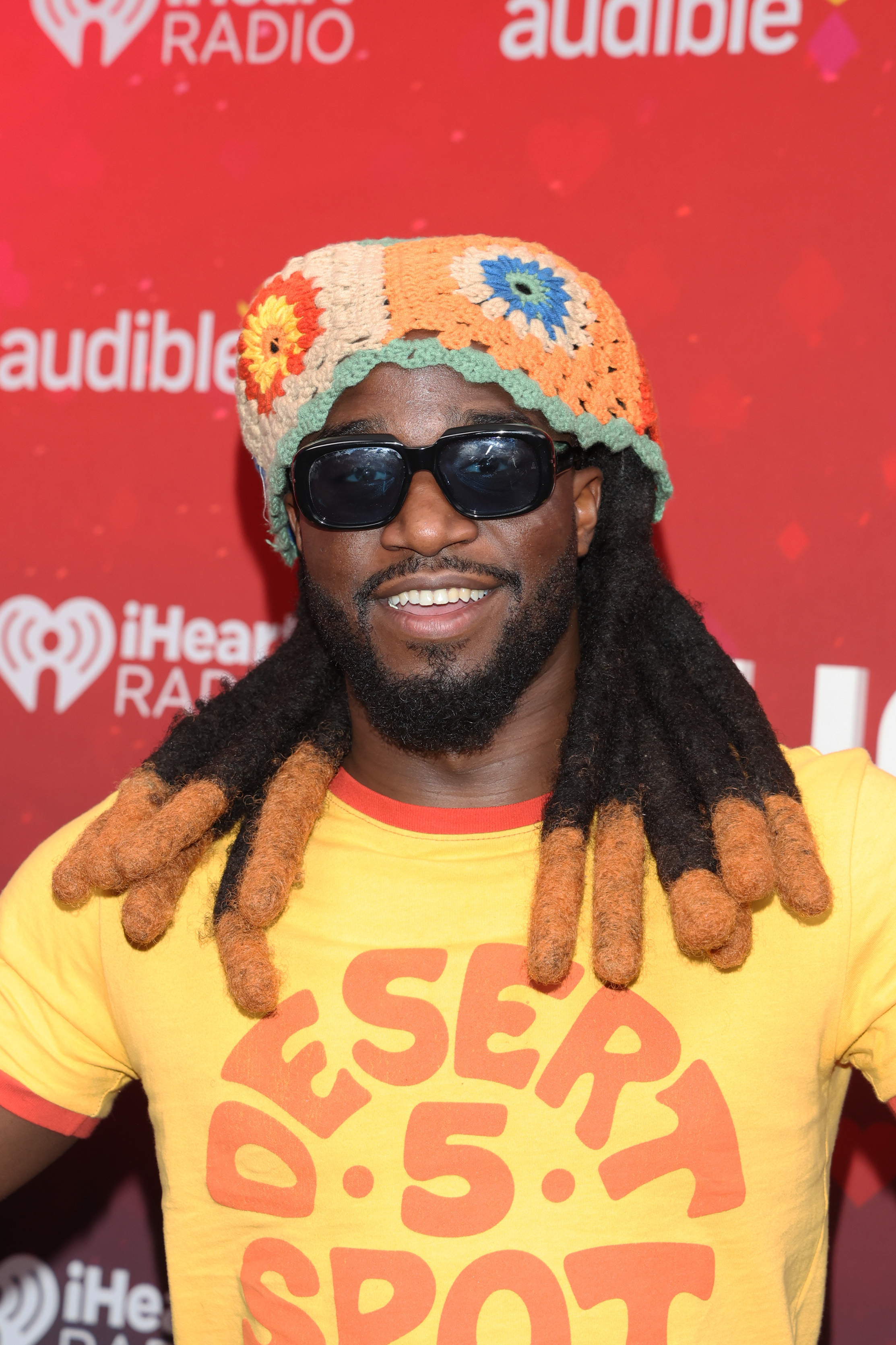 Man in crochet hat and sunglasses on a red carpet, wearing a yellow 