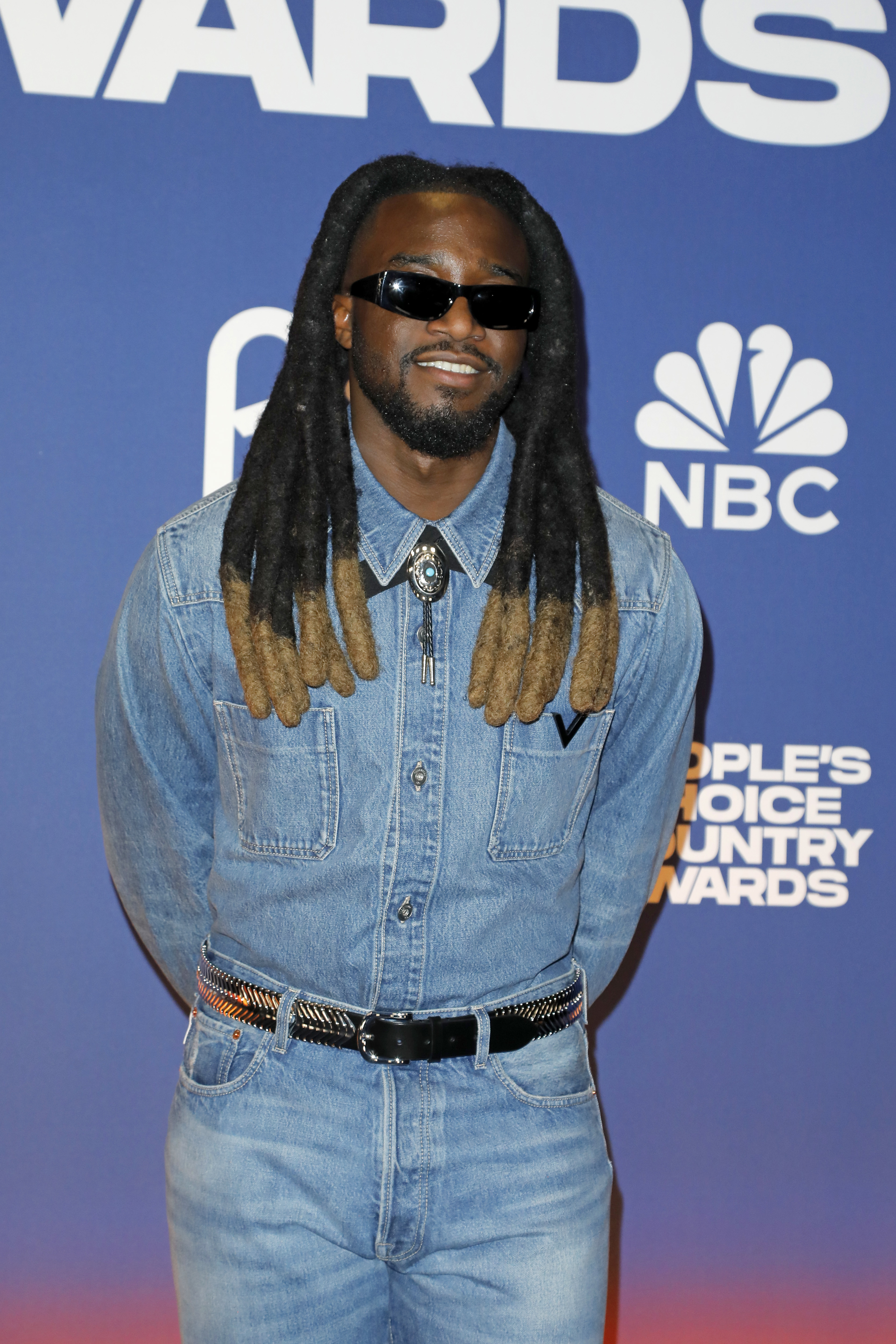 I don't know who this is. Person on red carpet wearing denim outfit, sunglasses, and a decorative belt. NBC and 