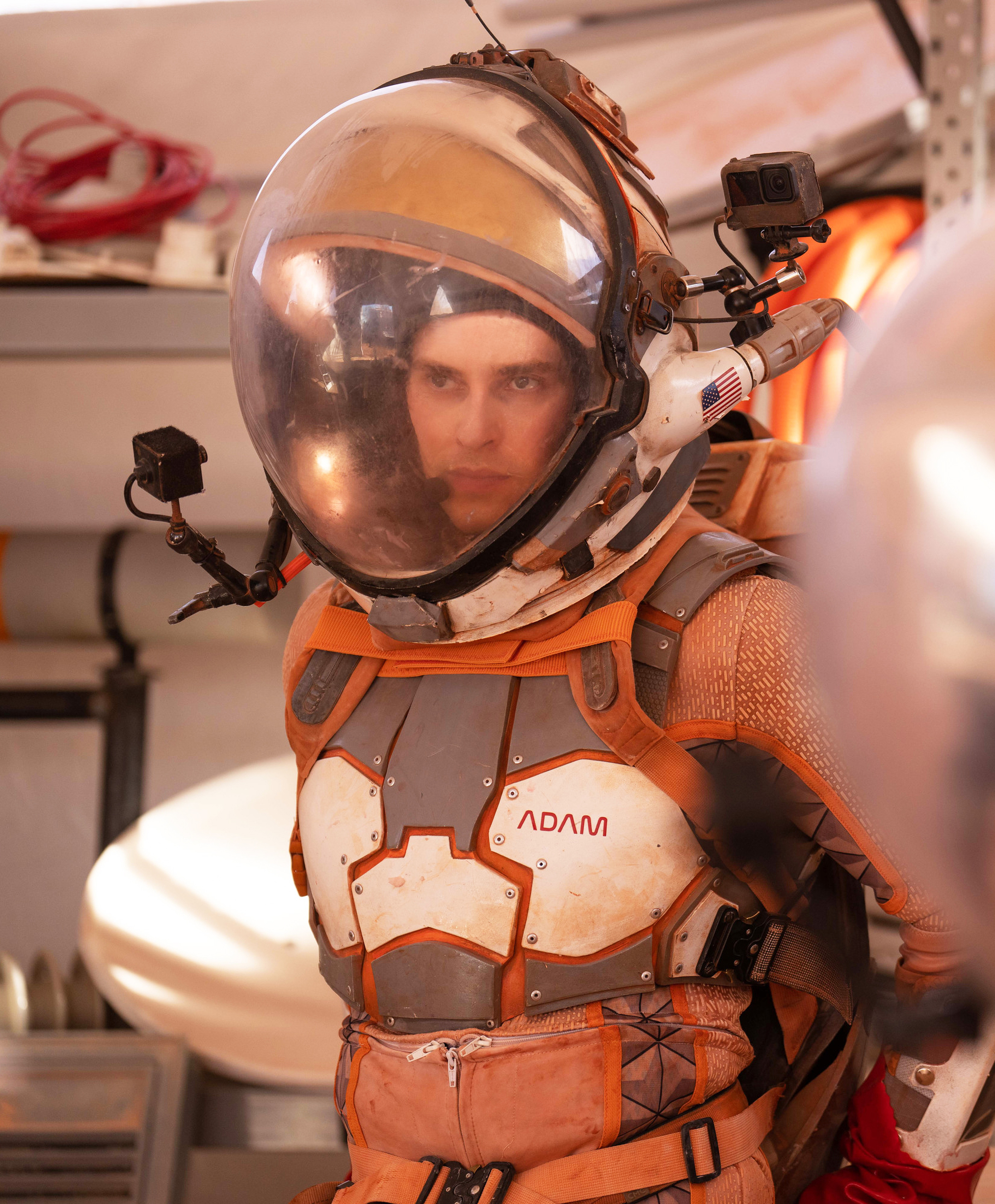 Adam Rippon in a space suit with a helmet labeled &quot;ADAM,&quot; standing inside a structure, for the show &quot;Stars on Mars&quot;.