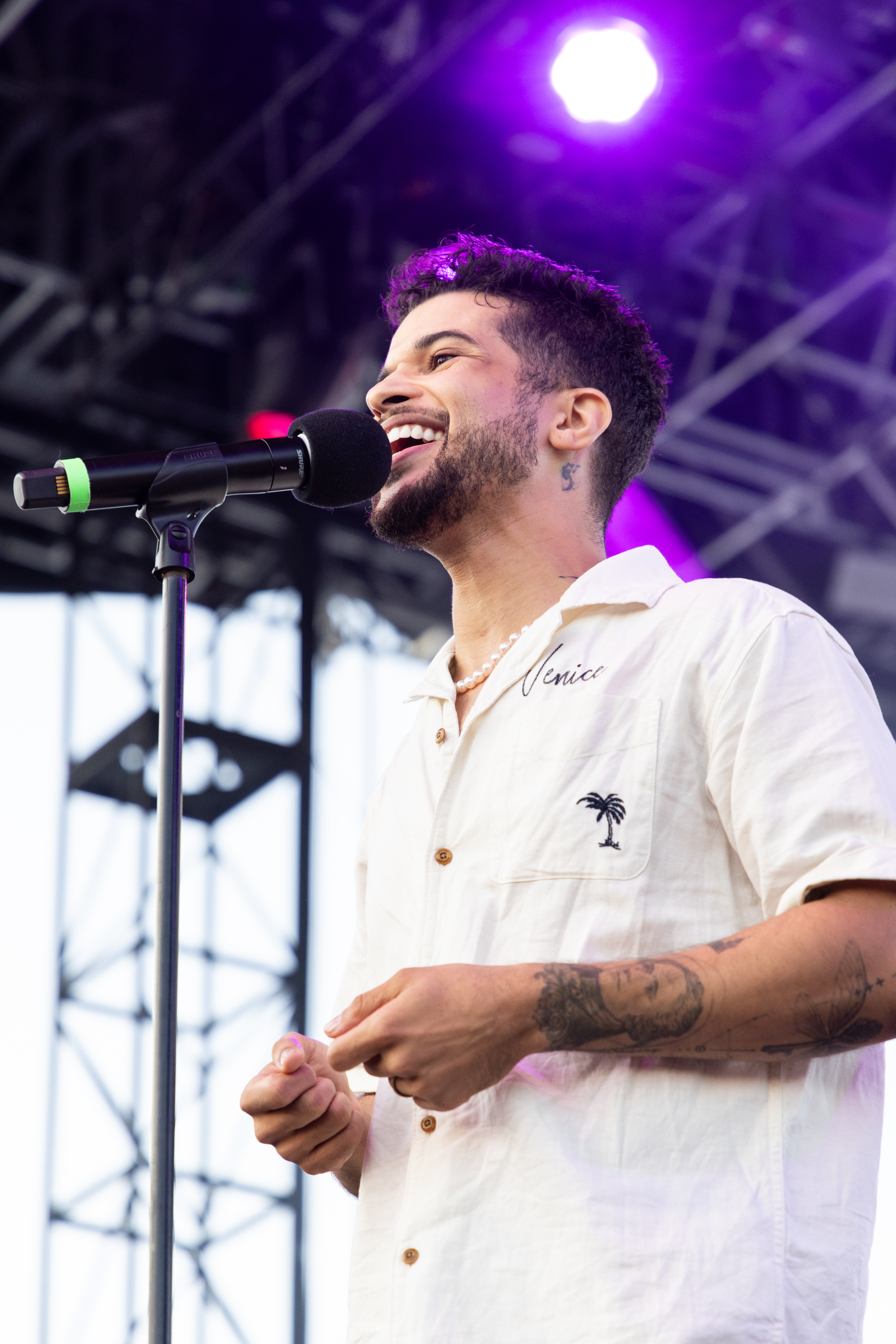 Jordan Fisher is singing on stage, wearing a casual shirt with a palm tree design