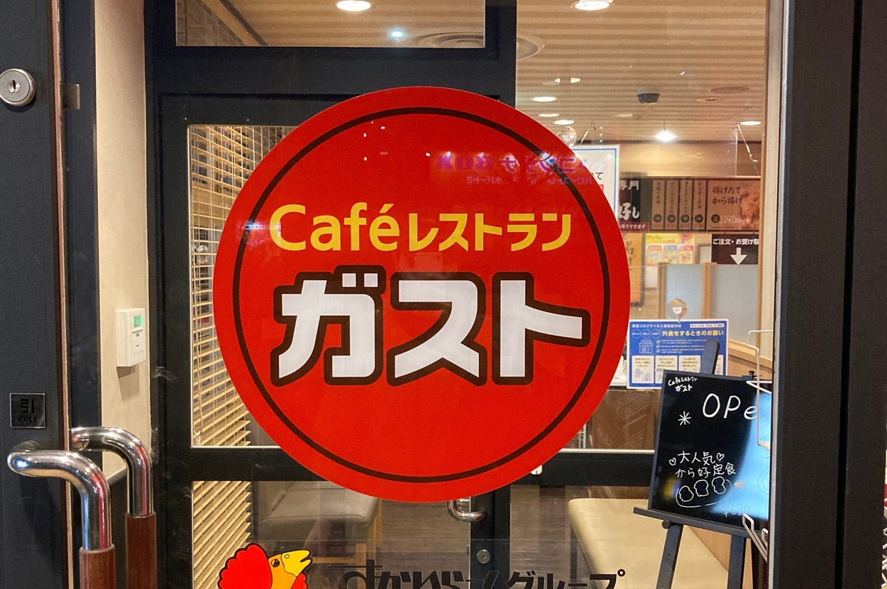 ガストのカフェレストラン入り口の写真。明るい赤いサインと営業中の黒板が見える。